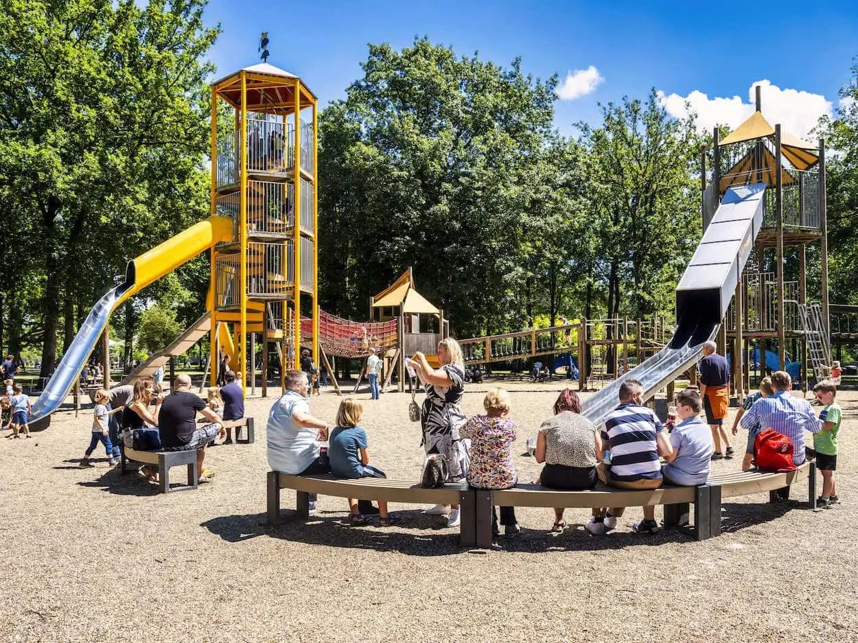 Grote avonturenspeeltuin in Bokrijk met hoge glijbanen, klimtorens en speeltoestellen omringd door volwassenen en kinderen op een zonnige dag