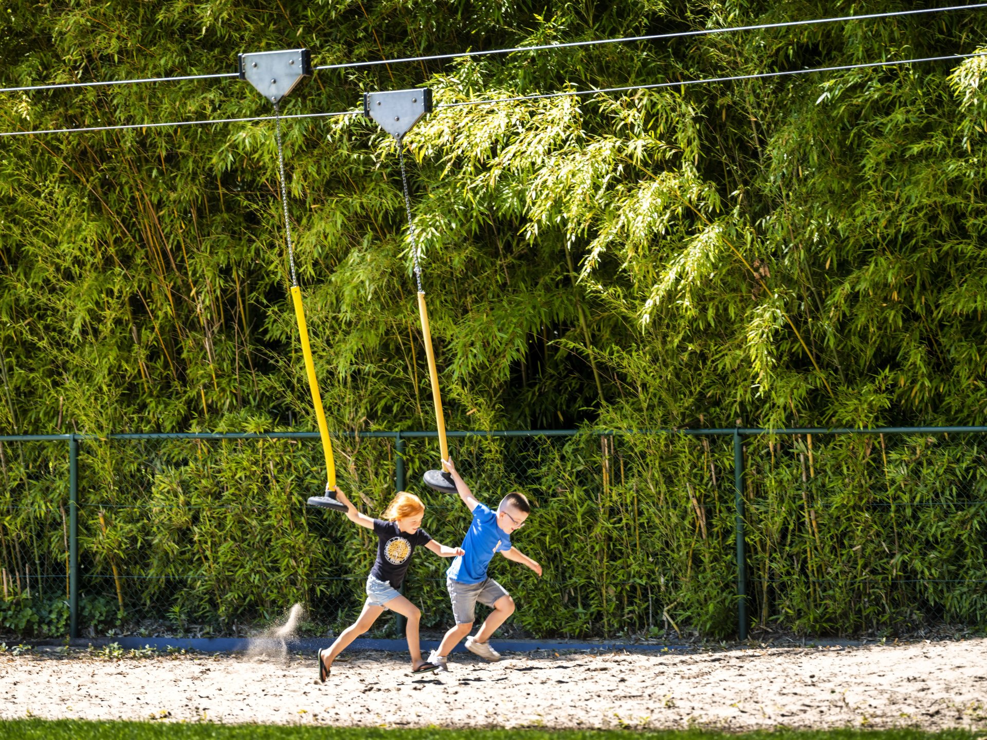 wee kinderen op een katrolglijbaan in de speeltuin van Bokrijk, spelend tussen groene bamboehaag