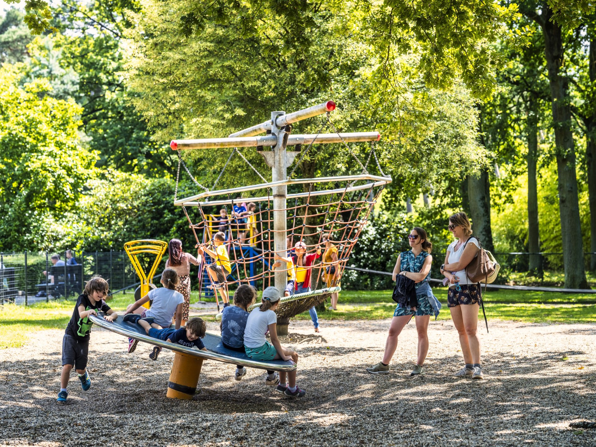 Kinderen spelen op een draaiend klimtoestel met touwnetten in de bosspeeltuin van Bokrijk, omringd door hoge bomen